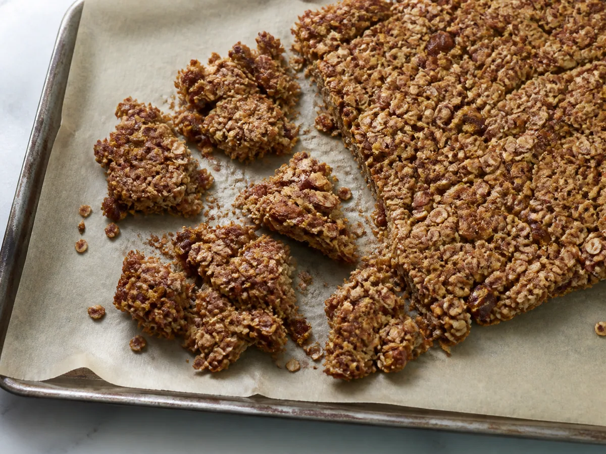 Lámina de granola con almendra y dátil completamente fría, rota en trozos grees e irregulares sobre el papel para hornear