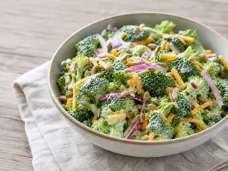 Tazón de ensalada cremosa de brócoli con pasas, cheddar, cebolla morada y semillas de girasol