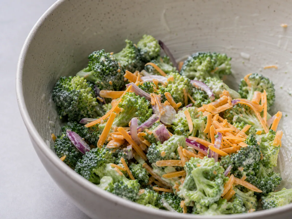 Broccoli salad evenly coated with dressing before sunflower seeds are added