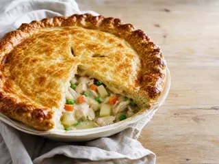 Pastel estadounidense de pollo con verduras de raíz y tapa de hojaldre dorada en una fuente de cerámica