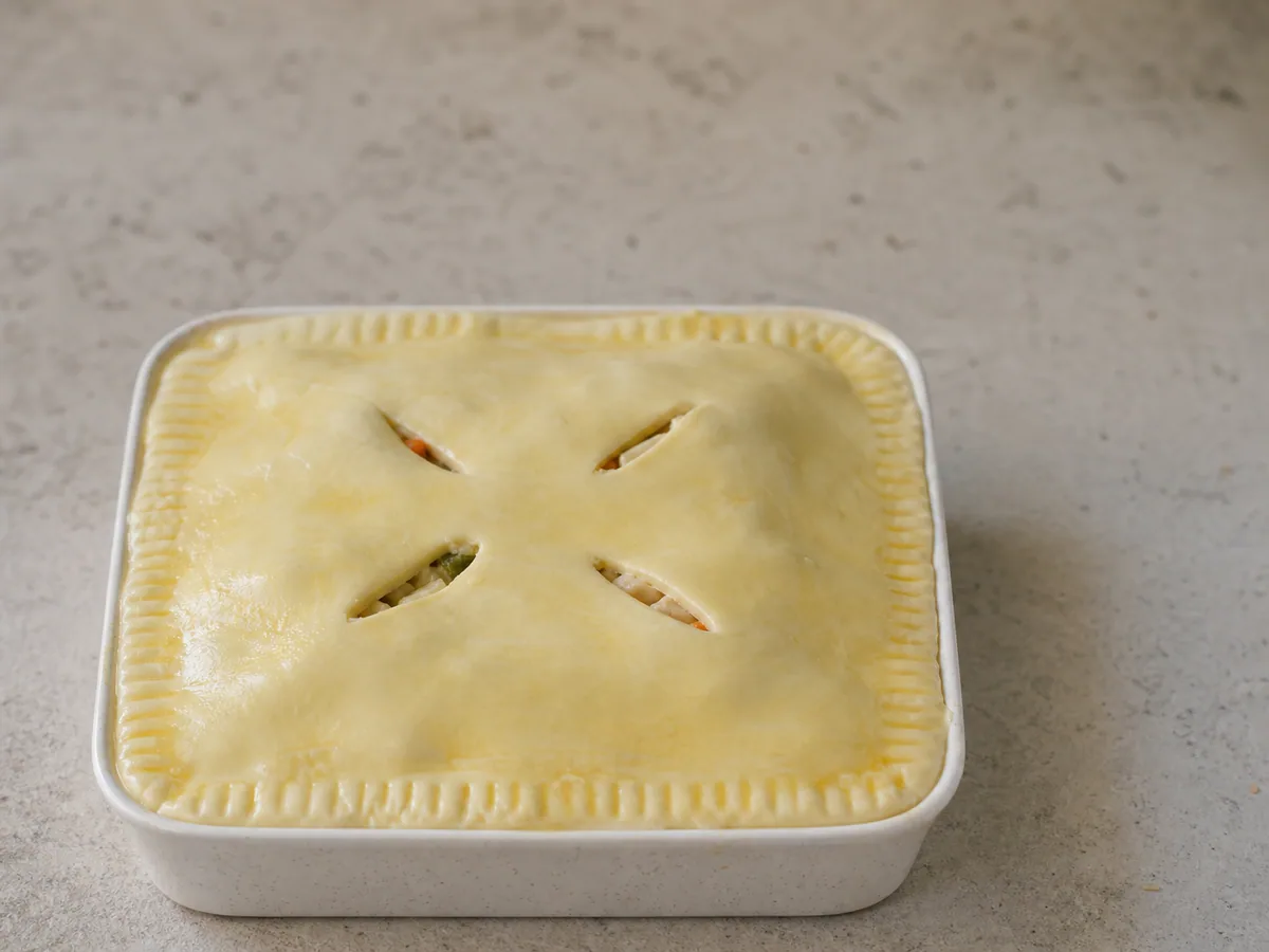 Puff pastry fitted over cooked chicken and root vegetable filling before egg wash