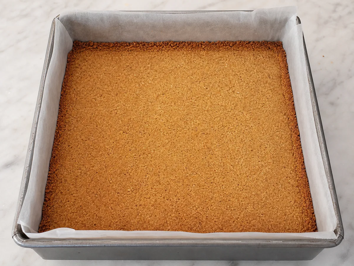 Baked graham cracker crust pressed level in a parchment-lined square pan