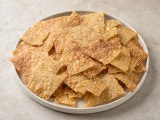 Fragmentos dorados de galleta de lavash con sésamo apilados en una fuente sencilla de cerámica