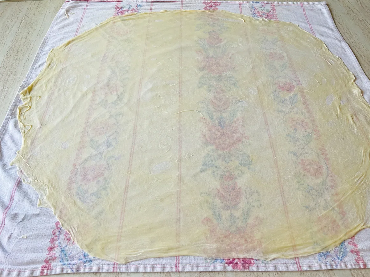 Translucent Austrian apple strudel dough stretched thin over a floured cloth