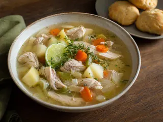 Bowl of Bahamian chicken souse with potatoes, carrots, lime, and Johnny cake