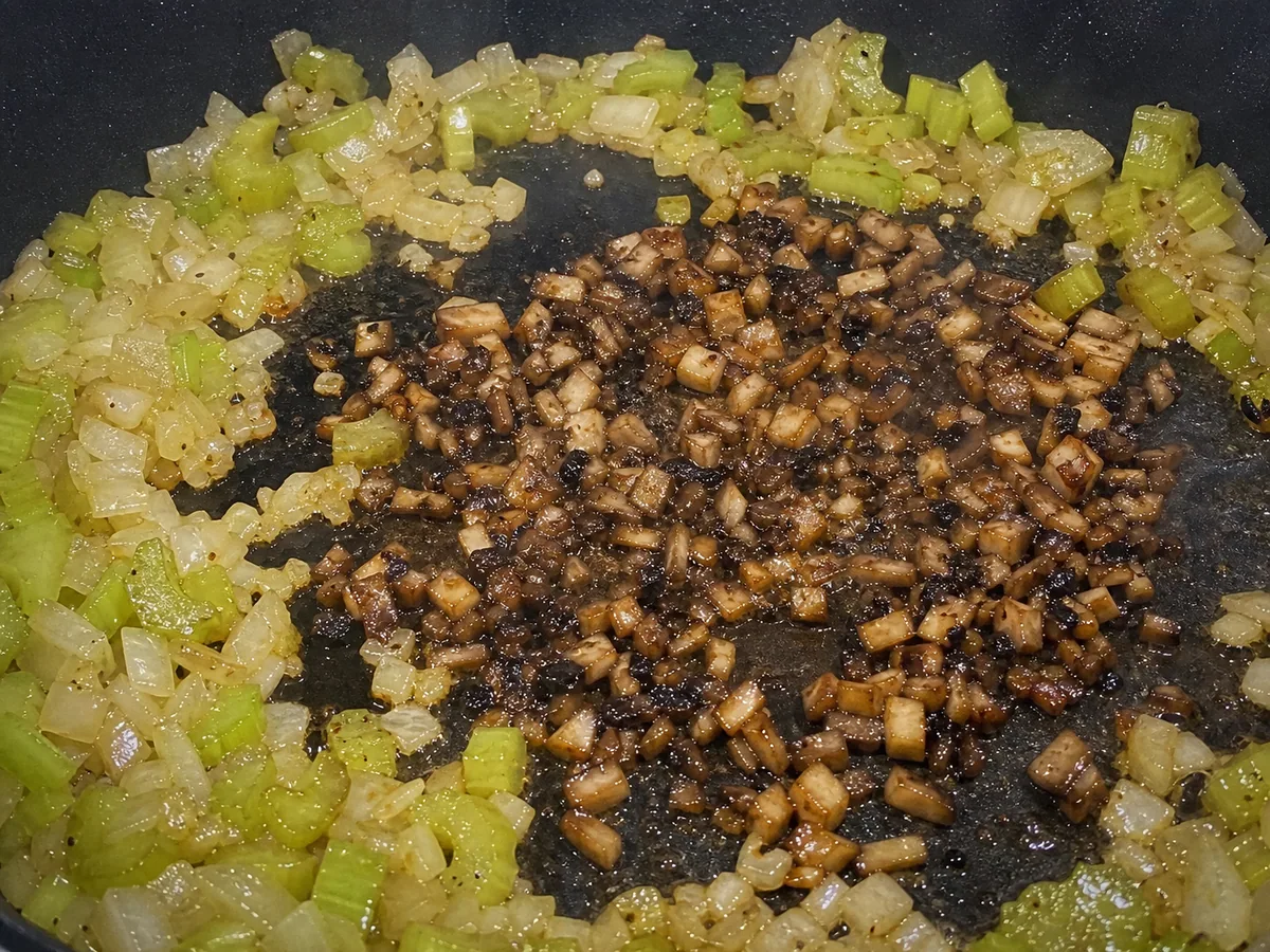 Well-browned cremini mushrooms with softened onion and celery in a wide skillet
