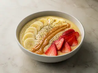 Banana peanut butter smoothie bowl topped with strawberries, banana slices, chia seeds, and peanut butter
