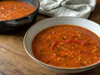 Tigela de sopa bósnia de tarhana com pimentos assados, salsinha e um pequeno redemoinho de creme azedo