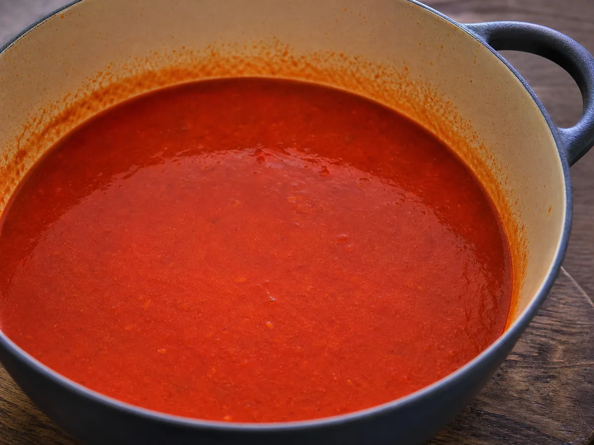 Mostly smooth brick-red roasted pepper broth in a pot for Bosnian tarhana soup