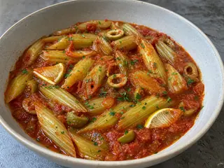 Shallow bowl of braised celery in tomato sauce with green olives and parsley