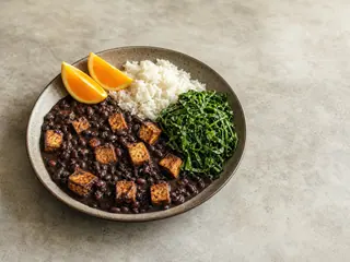 Brazilian black bean feijoada with smoked tofu, rice, collard greens, and orange wedges