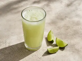 Glass of pale green Brazilian limeade with fine creamy froth and ice cubes
