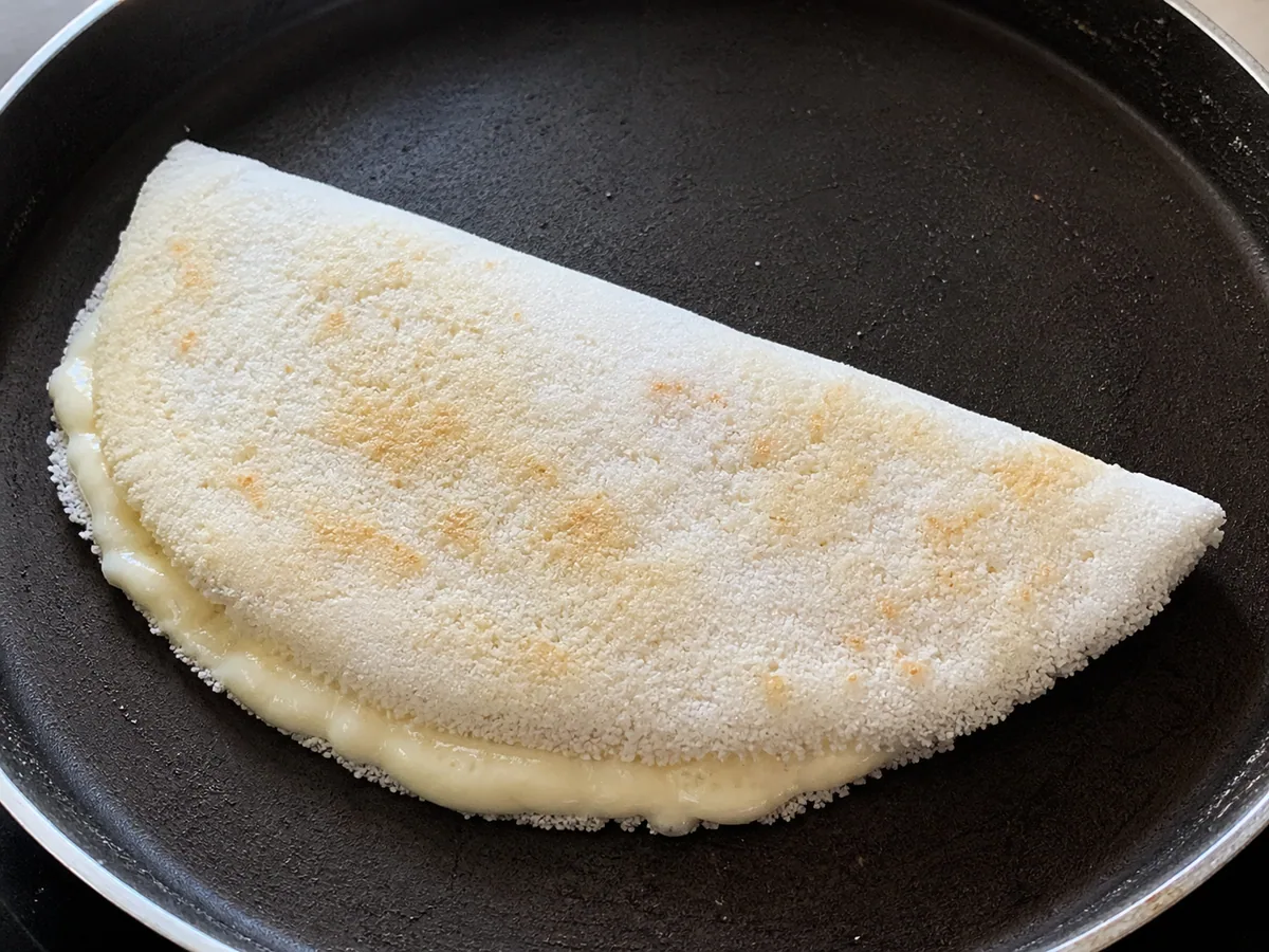 Crepa de tapioca doblada termineo de cocinarse en la sartén, con queso derretido asomeo por el pliegue
