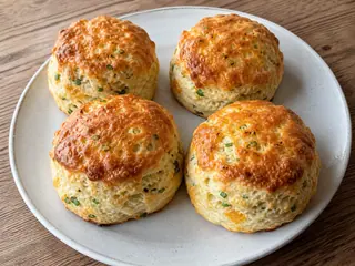 Scones británicos redondos de cheddar y cebollino, con superficie dorada y motas visibles de cebollino