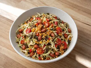 Tazón de ensalada birmana de hojas de té con repollo, tomates, maní, sésamo, garbanzos partidos y ajo frito