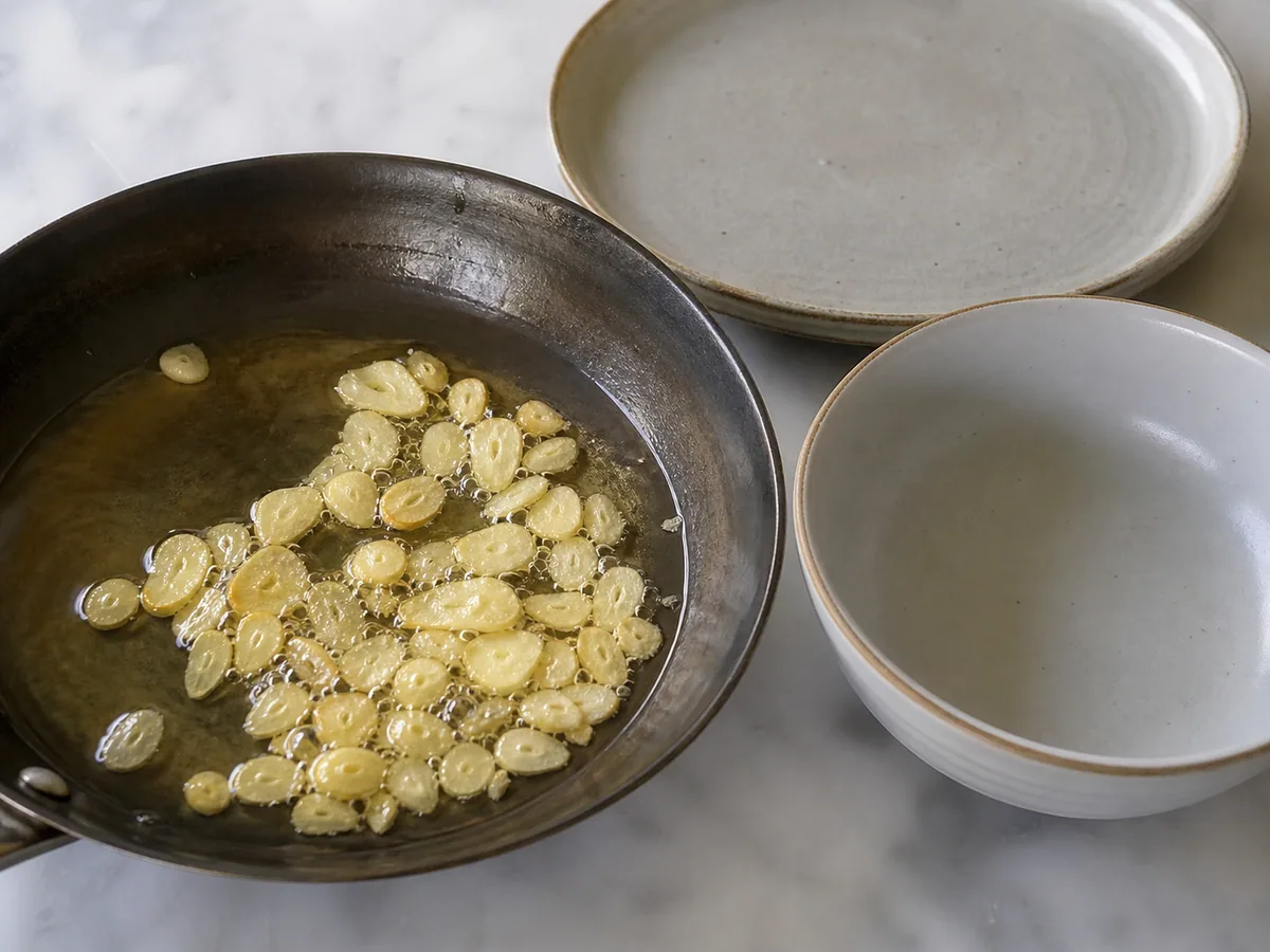 Rebanadas de ajo dorado claro burbujeeo suavemente en aceite de maní antes de retirarlas de la sartén