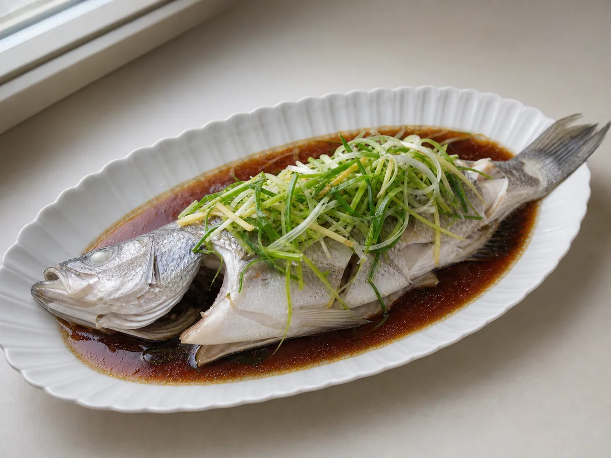 Cooked Cantonese steamed sea bass drained and topped with fresh ginger and scallions before hot oil