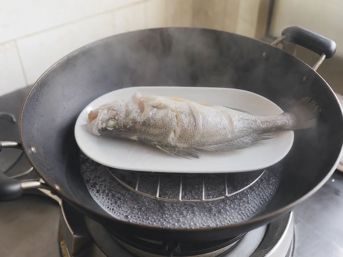 Fully cooked Cantonese steamed whole sea bass with opaque flesh in a wok steamer