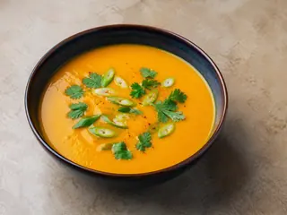 Tazón de sopa caribeña de calabaza y coco, cubierto con cebollín y cilantro