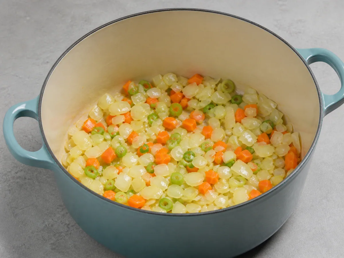 Cebola translúcida, cenouras amacieo e cebolinha na panela para a sopa caribenha de abóbora com coco