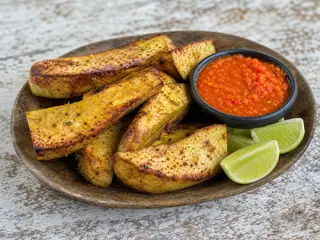 Gajos dorados de fruta de pan asada junto a un tazón de salsa caribeña de chile