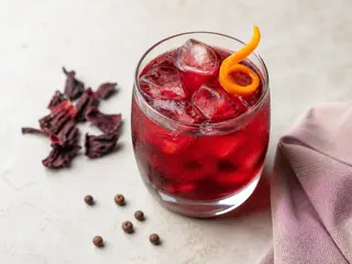 Vaso de bebida caribeña de flor de jamaica color rubí servido con hielo y cáscara de naranja