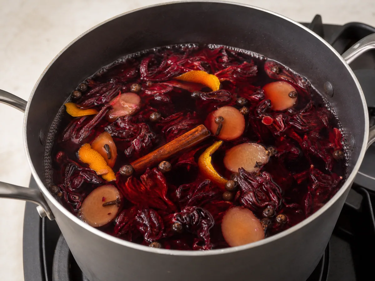 Bebida caribeña de flor de jamaica cocinándose a fuego lento con jengibre, cáscara de naranja y especias enteras en una olla