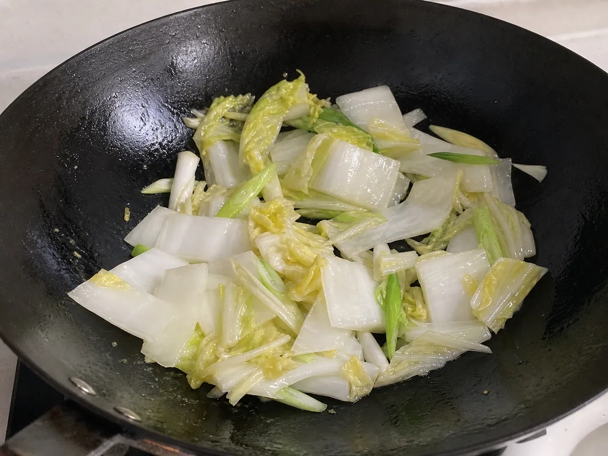 Nervuras brilhantes de repolho Napa e partes claras de cebolinha recém-amaciadas numa wok