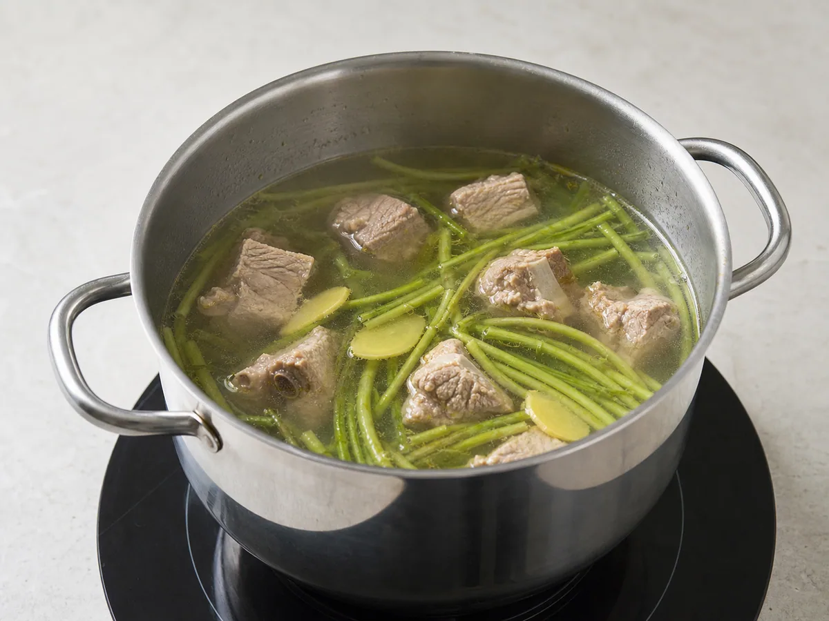 Fully cooked pork ribs simmering with softened watercress stems in clear broth