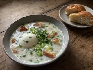 Bowl of Colombian changua with a fully cooked egg, bread, scallions, and cilantro