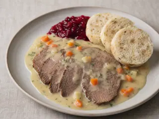 Carne de res checa braseada en rebanadas con salsa cremosa de verduras de raíz, dumplings de pan, conserva de arándano rojo y limón