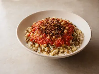 Bowl of Egyptian koshari topped with tomato sauce, chickpeas, and crisp onions