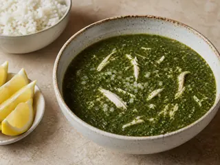Bowl of vivid green Egyptian molokhia chicken soup with tender chicken and lemon