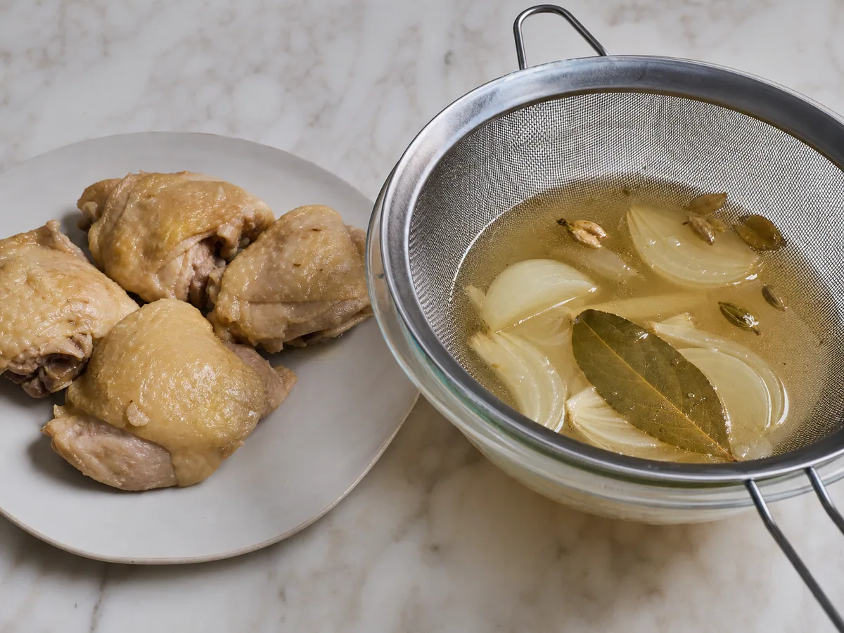 Sobrecoxas de frango totalmente cozidas em um prato limpo ao lado de caldo coado, prontas para desfiar