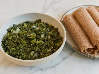 Bowl of Ethiopian collard greens with softened onions and jalapeno, served beside rolled injera