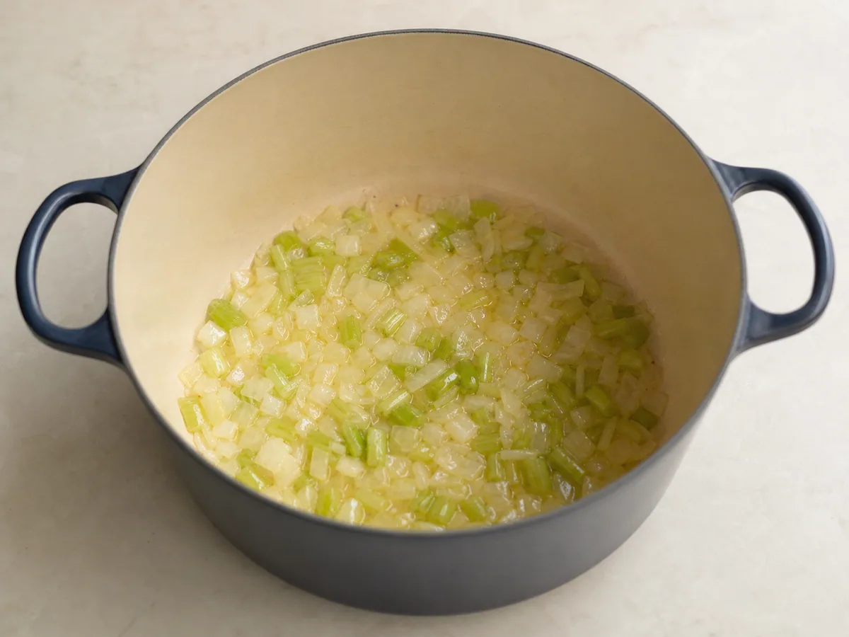 Cebolla amarilla y tallos de berza tiernos que comienzan a dorarse en una olla amplia