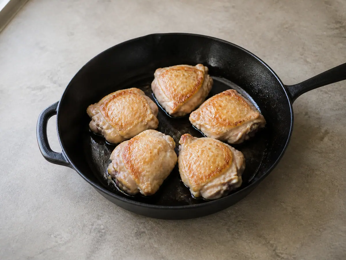 Chicken thighs browning on their second side in a black skillet