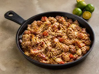 Sartén chisporroteante de sisig de cerdo crujiente con huevo bien cocido, cebollas, chiles y calamansi