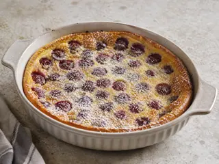 Clafoutis francés dorado de cerezas espolvoreado con azúcar glas en una fuente de cerámica