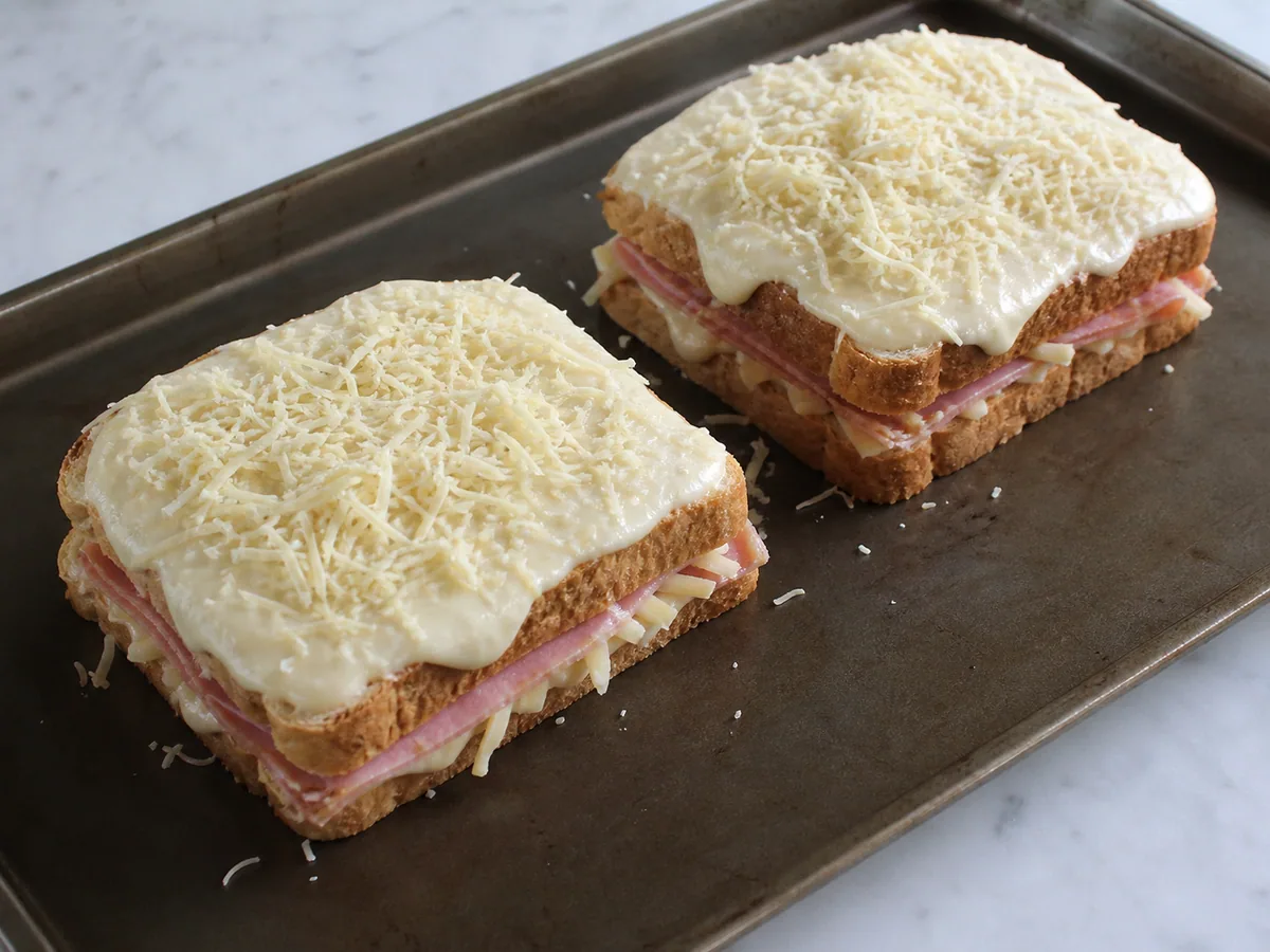 Four assembled croque madame sandwiches covered with béchamel and Gruyère before baking