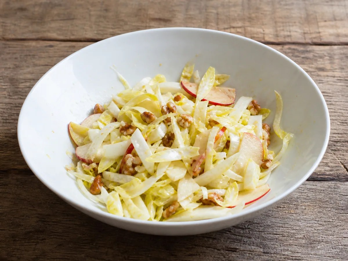 Salada francesa de endívias, maçã e nozes pronta na tigela, com nozes tostadas e lascas de Comté