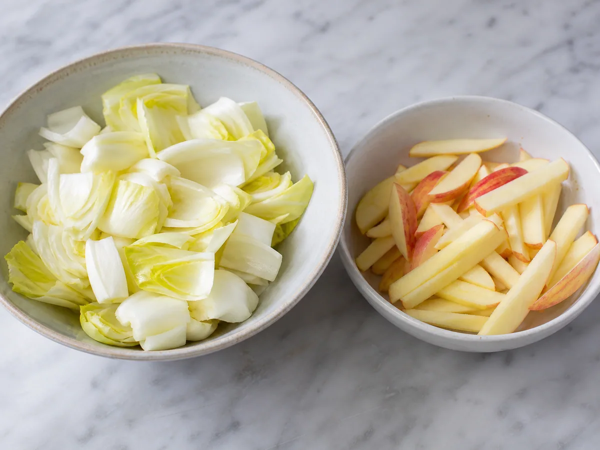 Folhas de endívia secas e palitos de maçã levemente envolvidos com vinagrete de Dijon para a salada francesa de endívias, maçã e nozes