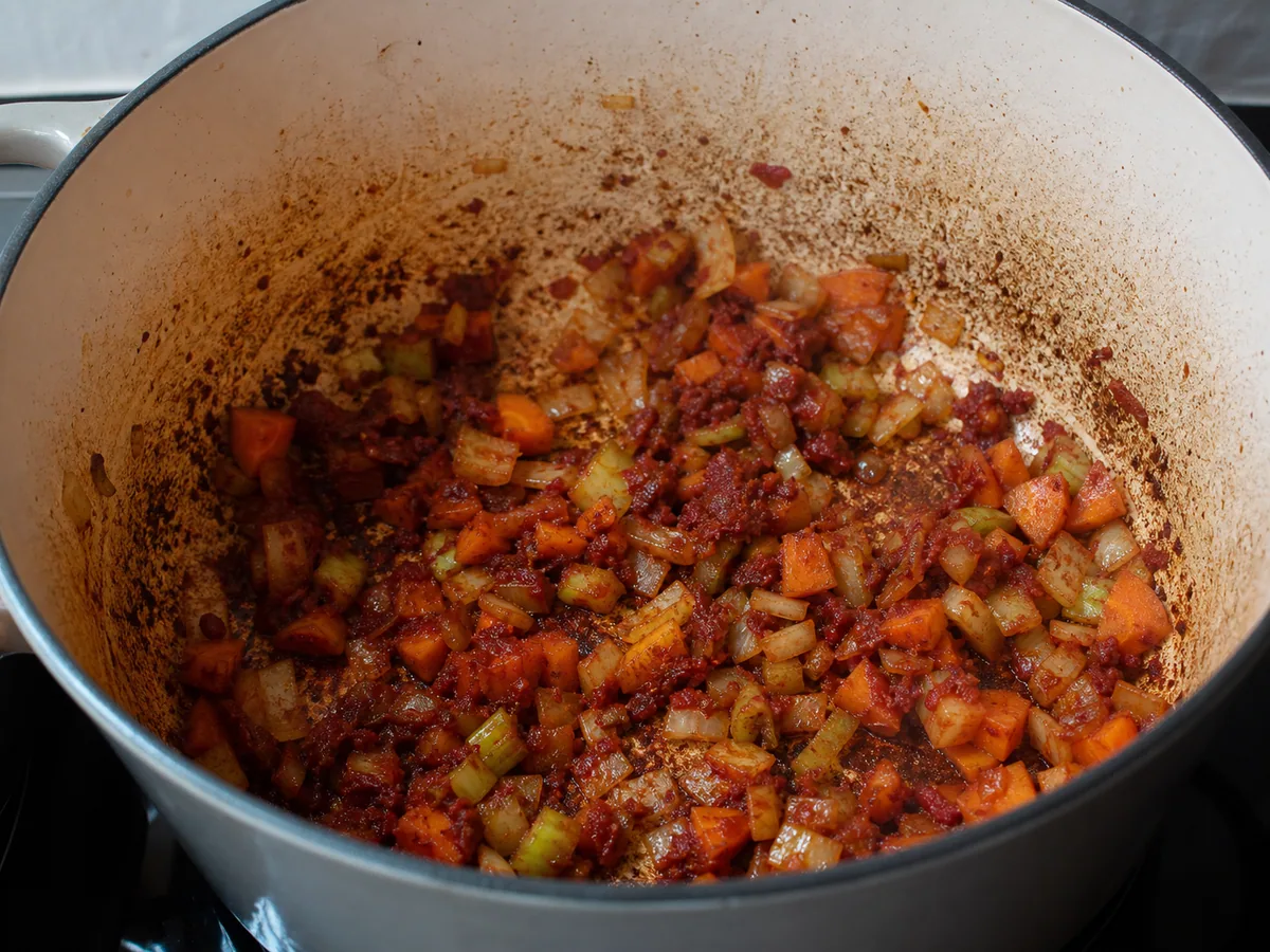 Softened onion, carrot, and celery with brick-red tomato paste in a Dutch oven