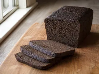 Fatias finas de pumpernickel alemão escuro ao lado de um pão denso de centeio integral