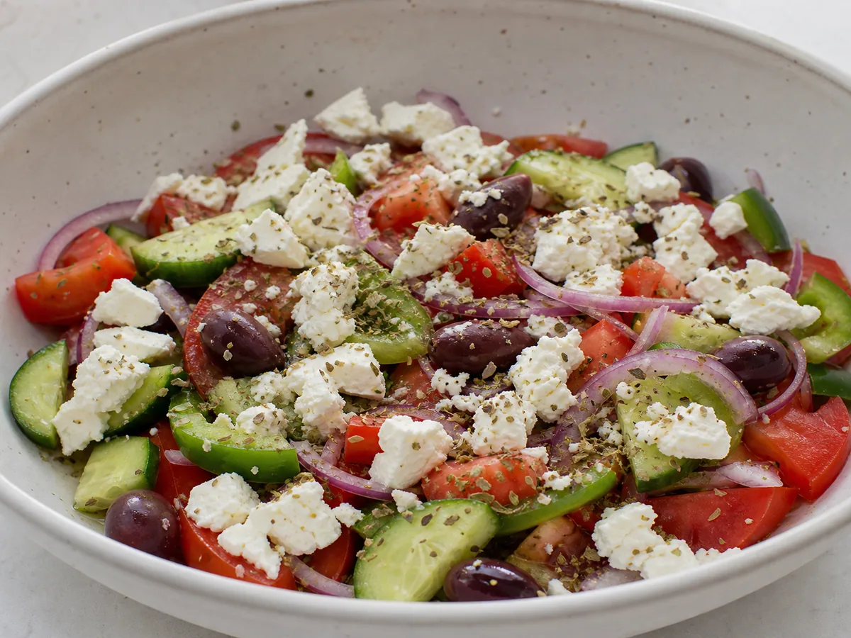 Salada grega camponesa coberta com pedaços grandes de feta e orégano reservado após receber o molho