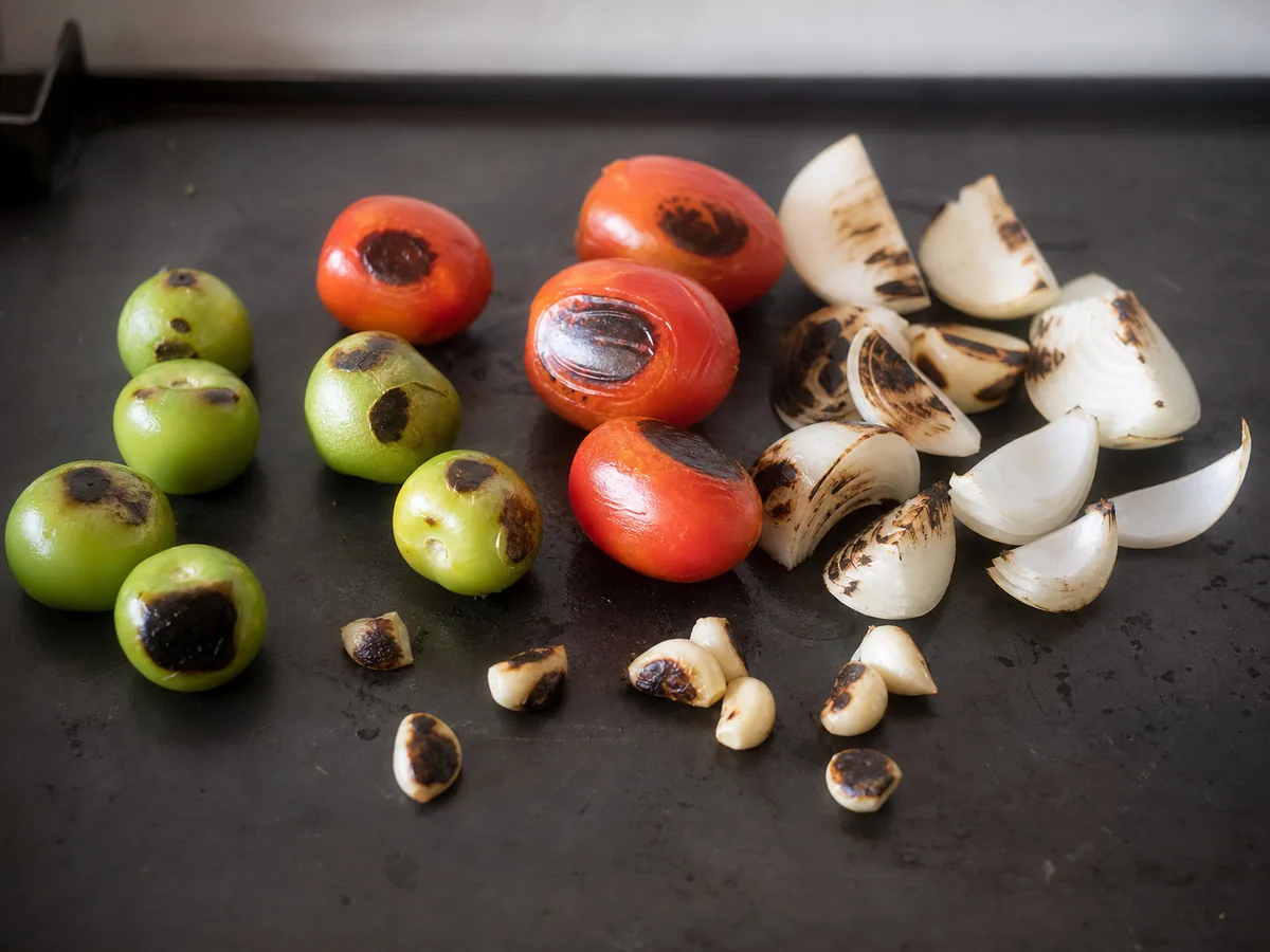 Tomates, tomatilhos, cebola e alho tostados para o recado do pepián guatemalteco de frango