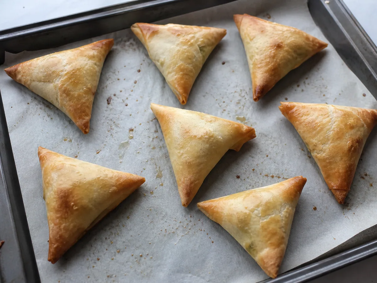 Samosas de legumes assadas, bem douradas e crocantes em uma assadeira