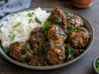 Chettinad pepper chicken in a shallow bowl with curry leaves and cilantro