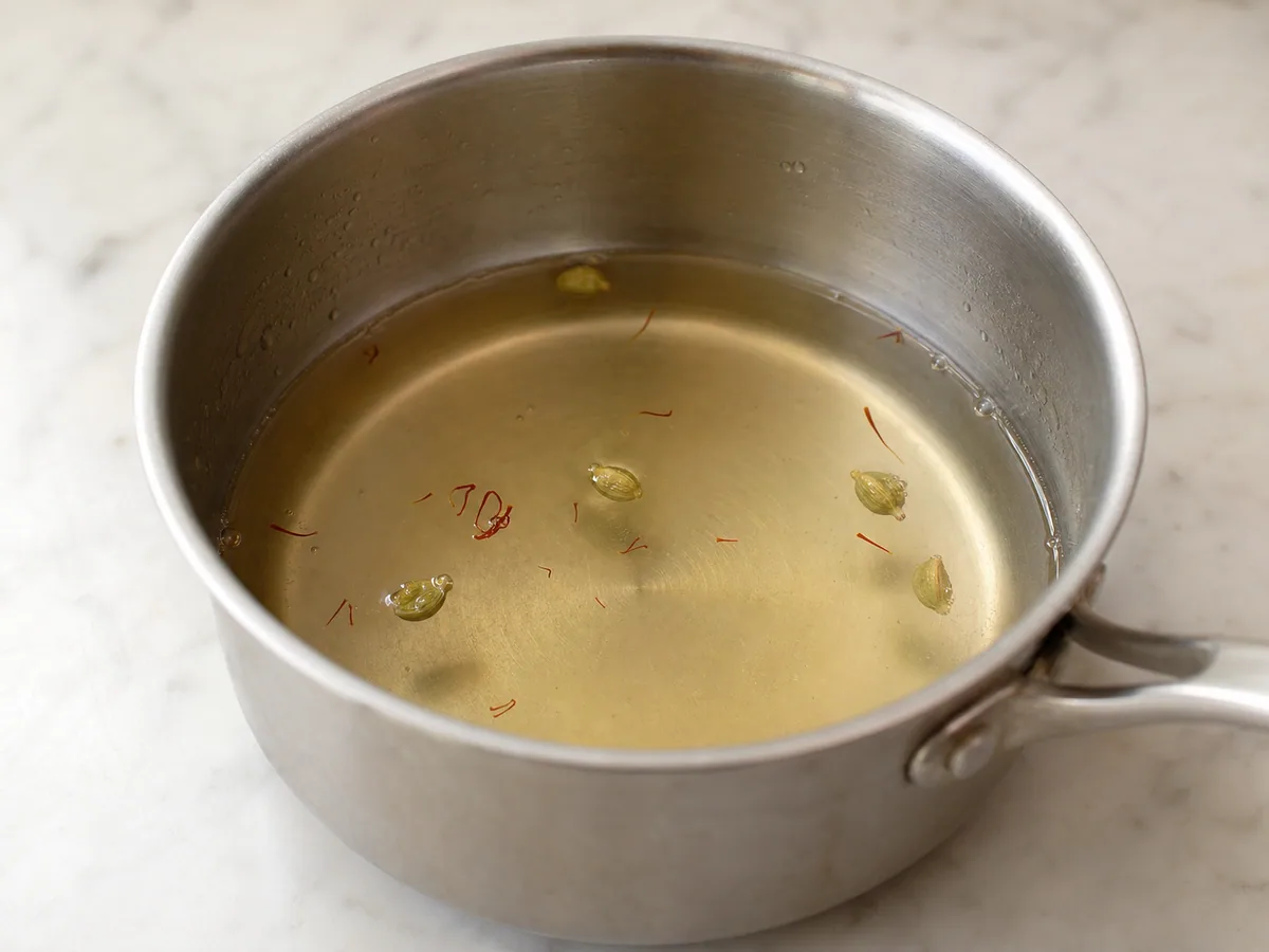 Almíbar fluido de cardamomo y agua de rosas cayendo en un hilo fino desde una cuchara