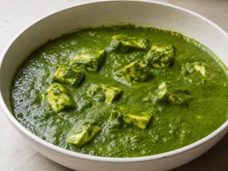 Tazón de palak paneer con cubos dorados de paneer en una salsa de espinaca de color verde intenso